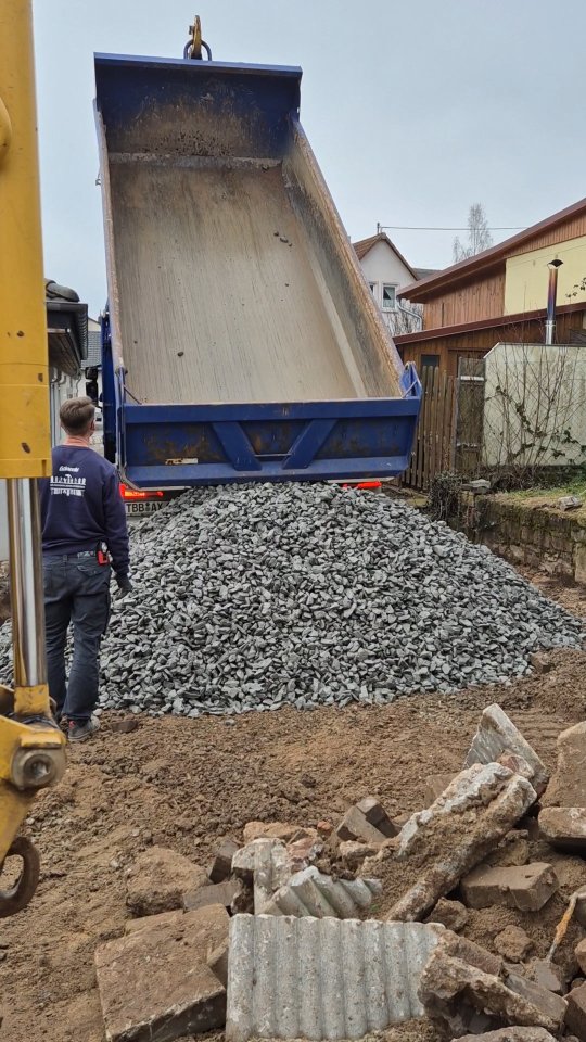 Lkw schüttet Schotter für den Unterbau einer Außenanlage ab, daneben ein Mitarbeiter von Albrecht